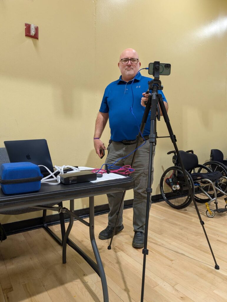 volinteer camera man with phone connected to laptop Volunteer Jeff recordining the live stream